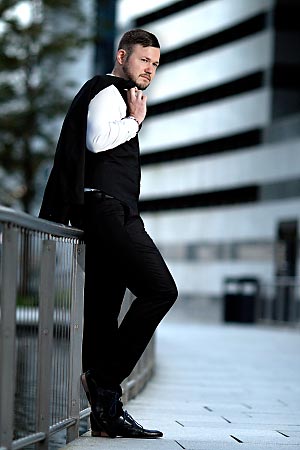 A young man wearing a suit is leaning on a guard railing.