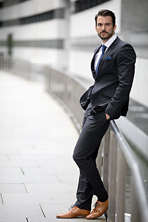 Ein junger Mann mit einem Anzug bekleidet lehnt sich an einem Geländer an.