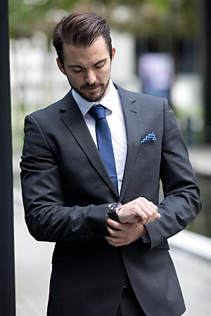 A young man wearing a suit is looking at his watch.
