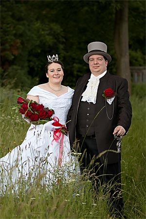 A bridal couple is standing in a hayfield.