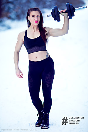 This photo shows a woman holding a barbell outside in a snowy landscape.